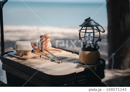 Camping essentials, a vintage kerosene lamp and a modern LED lantern on a wooden table. Enjoy nature, picnic, and a touch of nostalgia. A bright idea for your outdoor adventure. Camping essentials, a vintage kerosene lamp and a modern LED lantern on a wooden table. Enjoy nature, picnic, and a touch of nostalgia. A bright idea for your outdoor adventure. 109571145