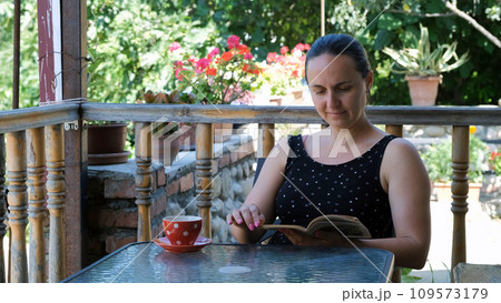Young woman reading interesting book while sitting on a terrace or balcony in summer day 109573179