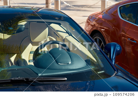 Two expensive sports cars stand side by side in sunny weather, a view of the bright interior through any glass 109574206