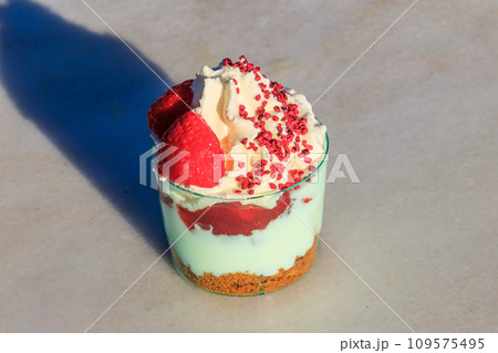 Strawberry trifle with whipped cream, berry sauce and cookie crumbs in a glass on a gray concrete background Strawberry trifle with whipped cream, berry sauce and cookie crumbs in a glass on a gray concrete background 109575495
