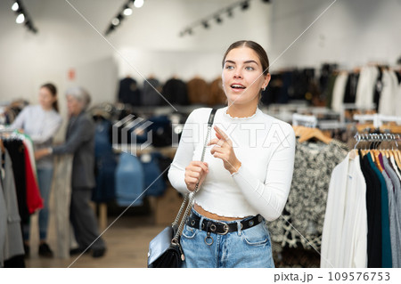 Positive joyful young woman looking for fashionable clothes in clothing boutique Positive joyful young woman looking for fashionable clothes in clothing boutique 109576753