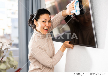 Asian woman wipes the dust from the TV with a rag 109576796
