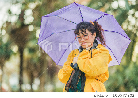 Cold winter rainfall. Throat pain and flu. Person sick. Latin mid woman with raincoat and umbrella Cold winter rainfall. Throat pain and flu. Person sick. Latin mid woman with raincoat and umbrella 109577802