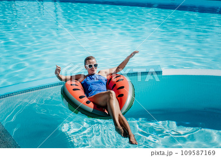Happy woman in a swimsuit and sunglasses floating on an inflatable ring in the form of a watermelon, in the pool during summer holidays and vacations. Summer concept. 109587169