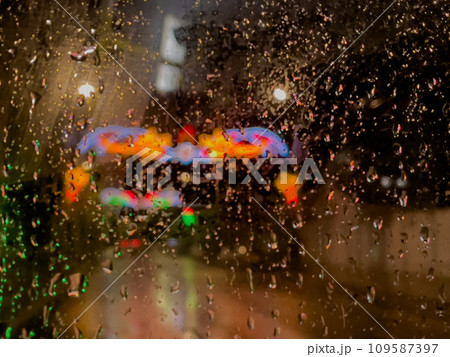 Rain bokeh road lights. Abstract shot of evening city traffic bokeh. Multicolored lights of the evening city and passing cars through a wet rainy window. 109587397