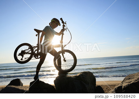 Woman carrying a folding bike on sunrise seaside road 109588420