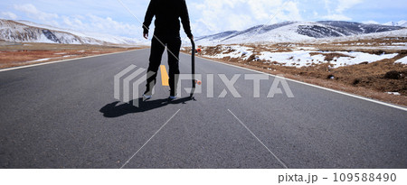 Skateboarder skateboarding on snowy country road 109588490