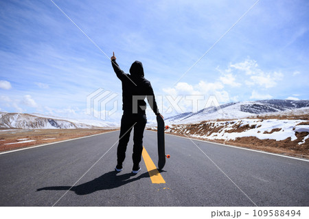 Skateboarder skateboarding on snowy country road 109588494