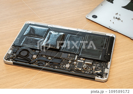Swollen battery of broken laptop in open casing closeup 109589172