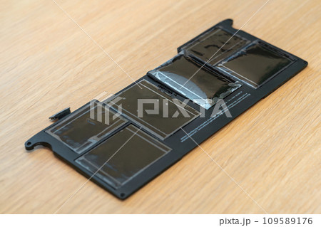 Swollen battery of broken laptop on wooden table closeup Swollen battery of broken laptop on wooden table closeup 109589176
