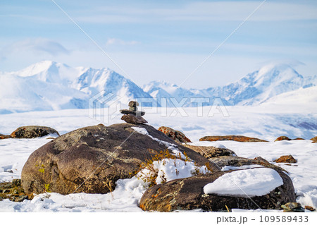 Cairn on a rock with the snow-covered Altai Mountains in the background under a clear sky. Cairn on a rock with the snow-covered Altai Mountains in the background under a clear sky. 109589433