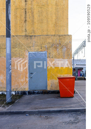 yellow wall of building and red street dumpster 109590529