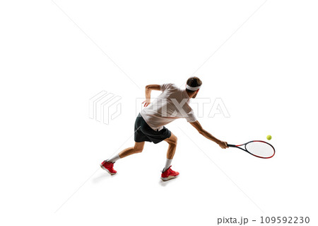 Dynamic image of concentrated young man, tennis player practicing, playing, hitting ball with racket isolated over white background. Sport 109592230