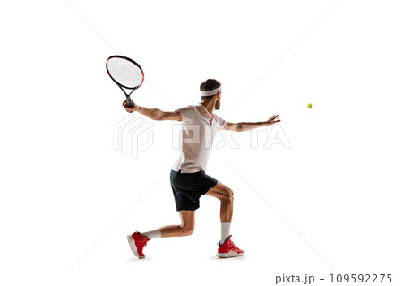 Concentered young man, tennis payer in motion during game, training, hitting ball with racket isolated over white background. Sport 109592275