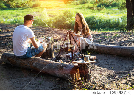 Young caucasian guy and girl sit on logs in nature and communicate. Outdoor recreation in summer, relaxation. 109592710