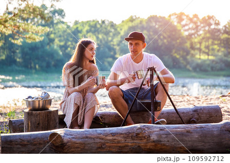 Young caucasian guy and girl sit on logs in nature and communicate. Outdoor recreation in summer, relaxation. 109592712