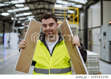 Portrait of young man with Down syndrome working in warehouse. Concept of workers with disabilities, support in workplace. 109593246