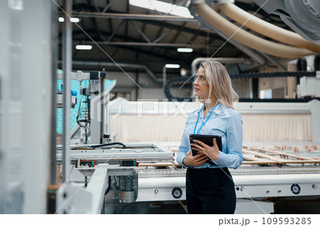 Female engineer in modern industrial factory, checking robotic arm, controling process and manufacturing equipment or machinery. Manufacturing facility with robotics and automation. 109593285