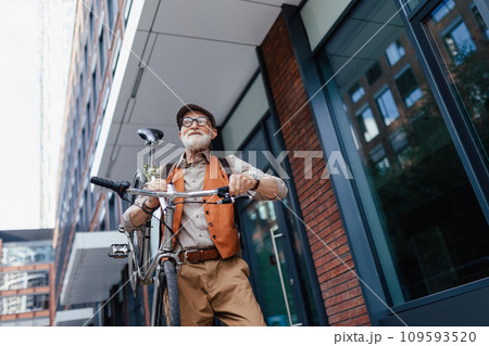 Elderly man, cyclist traveling through the city by bike, carrying bicycle on shoulder. Senior city commuter riding a bike. Elderly man, cyclist traveling through the city by bike, carrying bicycle on shoulder. Senior city commuter riding a bike. 109593520