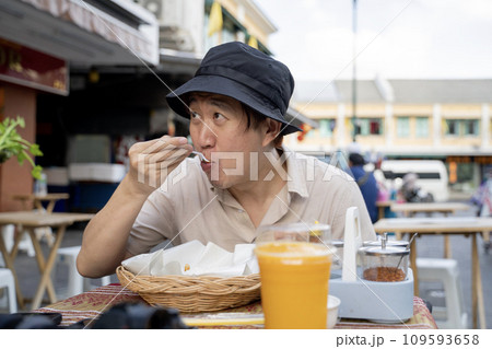 Solo travel food experience: Asian male tourist backpacker eating traditional Thai street food in Bangkok, Thailand 109593658