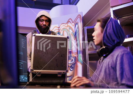 African american hacker opening black box with malicious ransomware program for data breach. Scammer showing case with illegal technology and planning hacking attack with crime partner 109594477
