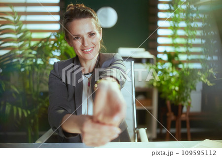 smiling business owner woman in green office stretching hands 109595112