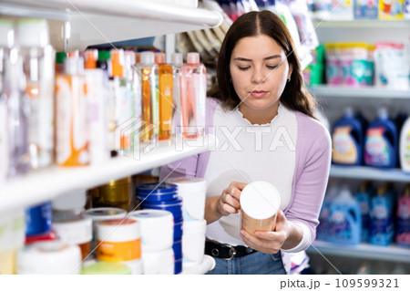 Female purchaser searching for reliable shampoo or conditioner in cosmetics store 109599321