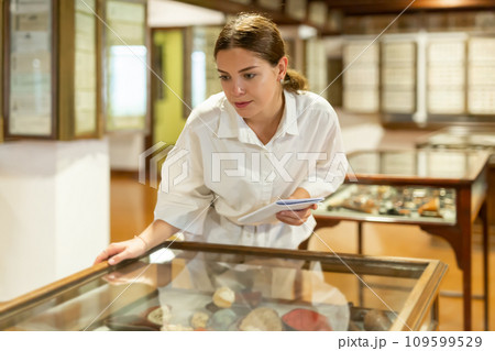 Young girl in the museum looks at the exposition behind glass case Young girl in the museum looks at the exposition behind glass case 109599529