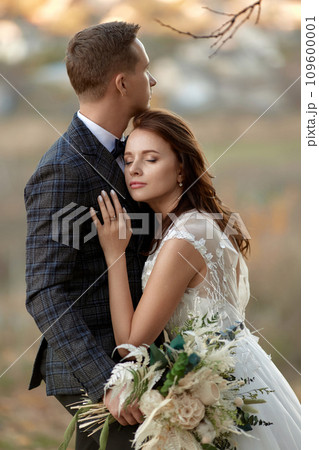 beautiful sensual bride in white wedding dress and groom standing outdoor on natural background 109600001