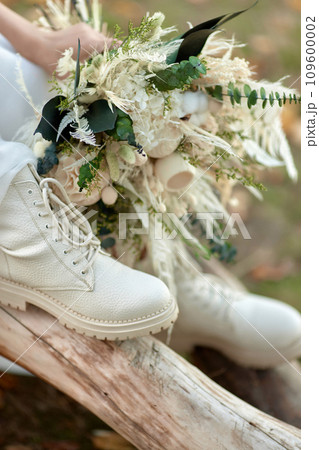 bride wearing white boots holding beautiful autumn bouquet. 109600002