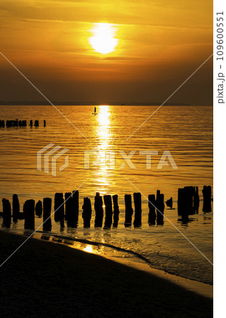 A man stands on a surfboard with a paddle in the middle of the sea. Sunset in the background. The concept of surfing. A man stands on a surfboard with a paddle in the middle of the sea. Sunset in the background. The concept of surfing. 109600551