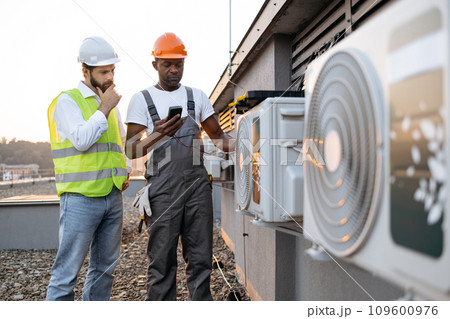 Two technicians standing with multimeter near cooling system Two technicians standing with multimeter near cooling system 109600976