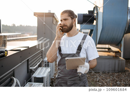 Man factory worker using tablet and talking on phone on roof Man factory worker using tablet and talking on phone on roof 109601684