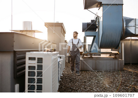 Craftsman walking by conditioners and holding tablet on roof Craftsman walking by conditioners and holding tablet on roof 109601707