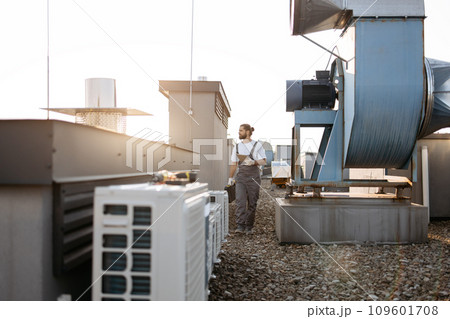 Craftsman walking by conditioners and holding tablet on roof Craftsman walking by conditioners and holding tablet on roof 109601708
