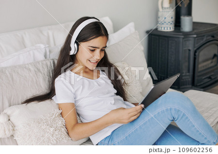 Preteen girl wear headphones using modern digital tablet at home Preteen girl wear headphones using modern digital tablet at home 109602256