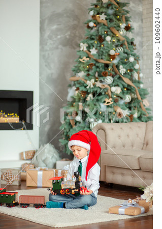 Happy little boy with a gift, toy train, under the Christmas tree on New Year's morning. Time to fulfill wishes. Happy little boy with a gift, toy train, under the Christmas tree on New Year's morning. Time to fulfill wishes. 109602440
