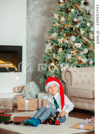 Happy little boy with a gift, toy train, under the Christmas tree on New Year's morning. Time to fulfill wishes. Happy little boy with a gift, toy train, under the Christmas tree on New Year's morning. Time to fulfill wishes. 109602443