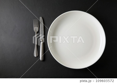 Empty white dinner plate and cutlery on a black stone table. Top view with copy space Empty white dinner plate and cutlery on a black stone table. Top view with copy space 109603572