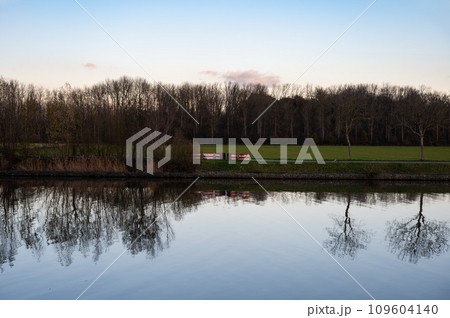 Bare trees reflecting in the calm water of the canal at dusk, Grimbergen, Belgium Bare trees reflecting in the calm water of the canal at dusk, Grimbergen, Belgium 109604140