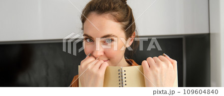 Close up portrait of cute girlfriend, giggle, reading notebook, holding planner and smiling at camera 109604840