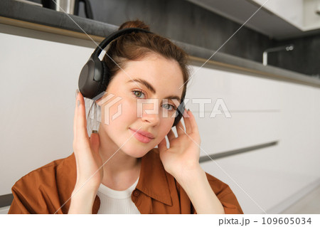 Close up portrait of beautiful brunette woman, listens to music in wireless headphones, has new earphones on her head, smiling and looking happy 109605034