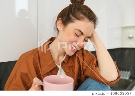 Cosy moments. Happy young woman sits in kitchen and drinks coffee, has tender smile on her face Cosy moments. Happy young woman sits in kitchen and drinks coffee, has tender smile on her face 109605057
