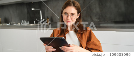 Portrait of busy young woman, self-employed entrepreneur sitting at home with digital tablet, reading documents. Student working on project remotely, holding gadget, studying 109605096