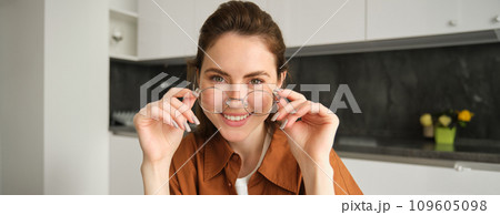 Portrait of young happy woman, sitting in kitchen, wearing glasses, reading or working from home 109605098