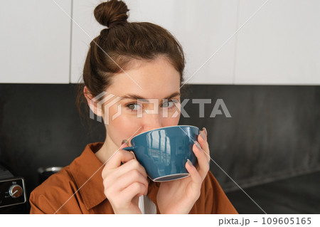 Close up portrait of beautiful, relaxed young woman, enjoying aroma of coffee, drinking cappuccino and smiling 109605165