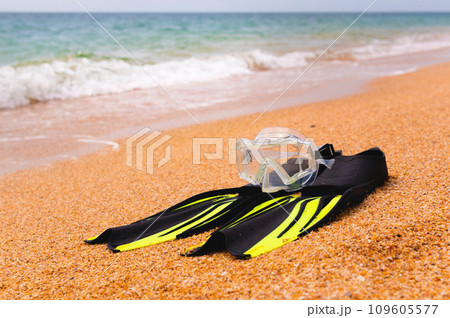 pair of fins and a diving mask on a sandy beach, bottom view. Space for text or advertising of a sports store or beach resort pair of fins and a diving mask on a sandy beach, bottom view. Space for text or advertising of a sports store or beach resort 109605577