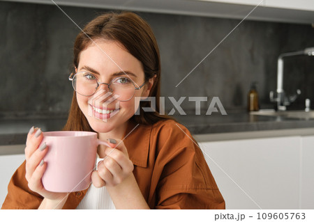 Close up portrait of cute smiling woman, spends time at home, sits in kitchen with cup of coffee, drinks tea, relaxes 109605763