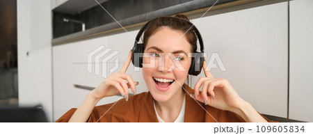 Carefree female model in wireless headphones, listens to music, enjoys favourite tunes in earphones, sings along and smiles 109605834