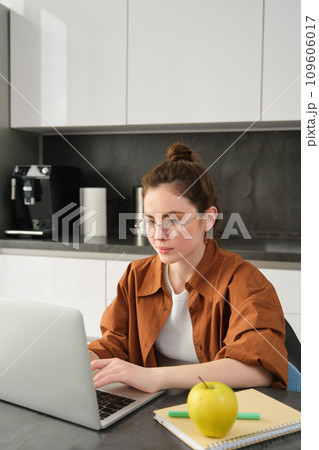Vertical shot of woman working from home, business owner using laptop, browsing social media on computer, wearing glasses 109606017